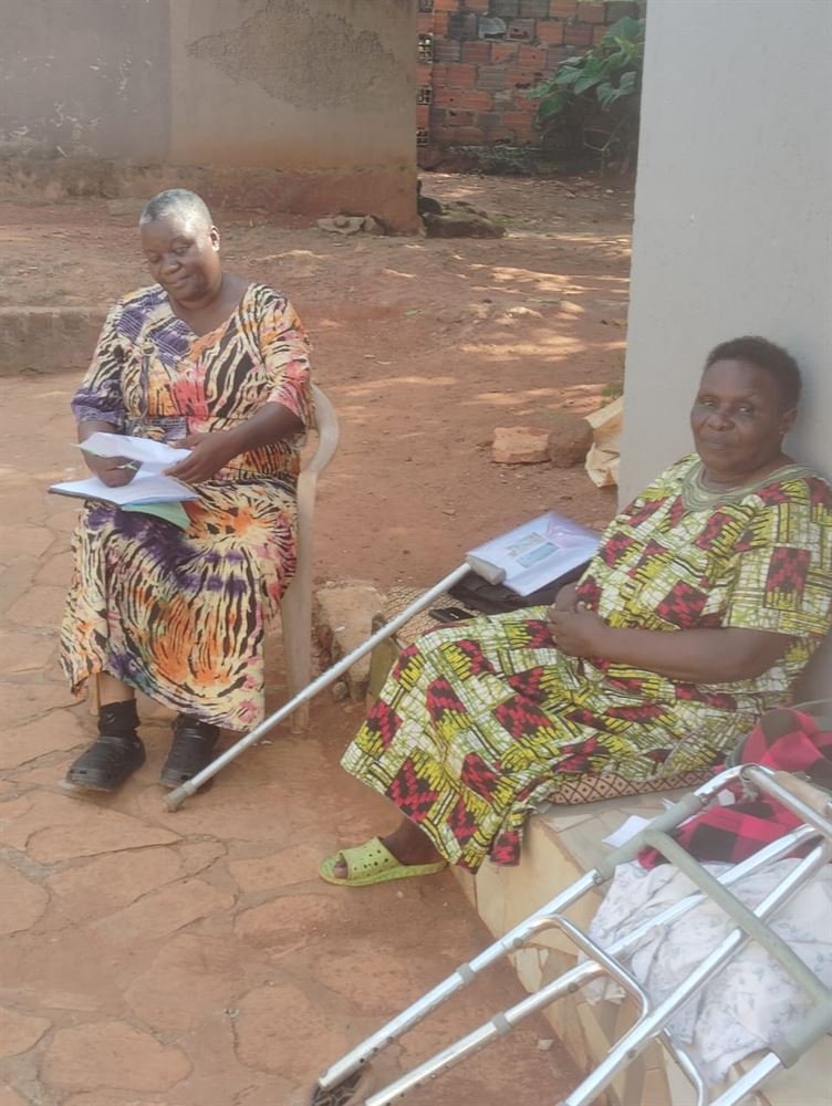 An RDAF team member sits with a community member and her walking frame during a home follow-up visit.