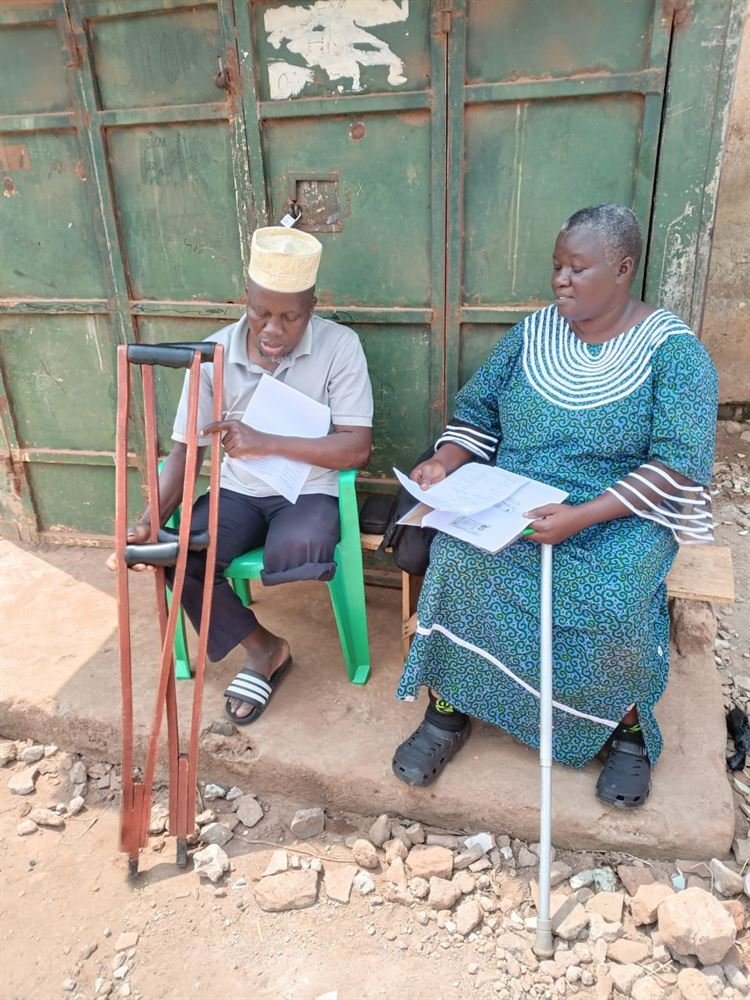 Two community members seated outdoors reviewing RDAF programme documents together.