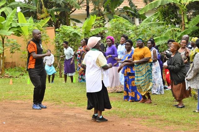Community members follow a leader through a warm-up exercise outdoors.