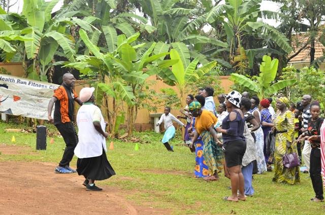 Community members gather on a village path beside a health and fitness banner.