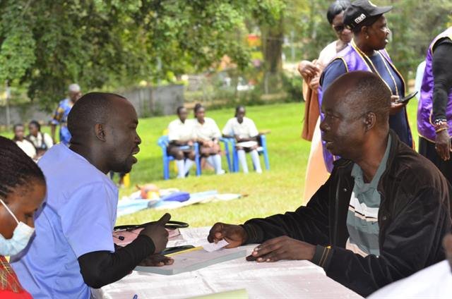 Community members register with RDAF staff at an outdoor table before screening.