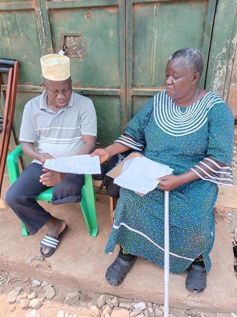 An RDAF team member sits with a community member outside his home, reviewing paperwork together.