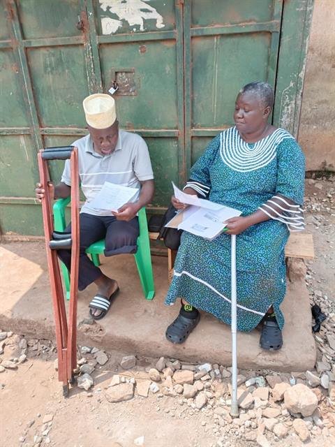 A man using elbow crutches and a woman with a walking stick read documents seated outside a home.