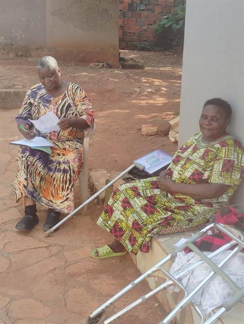 A woman with a walking frame sits beside another community member reading documents.