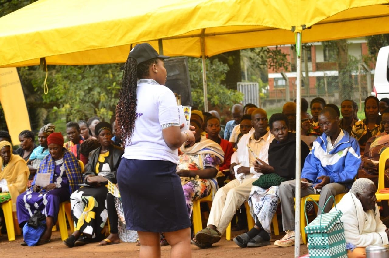 A facilitator addresses community members seated together under an event tent.