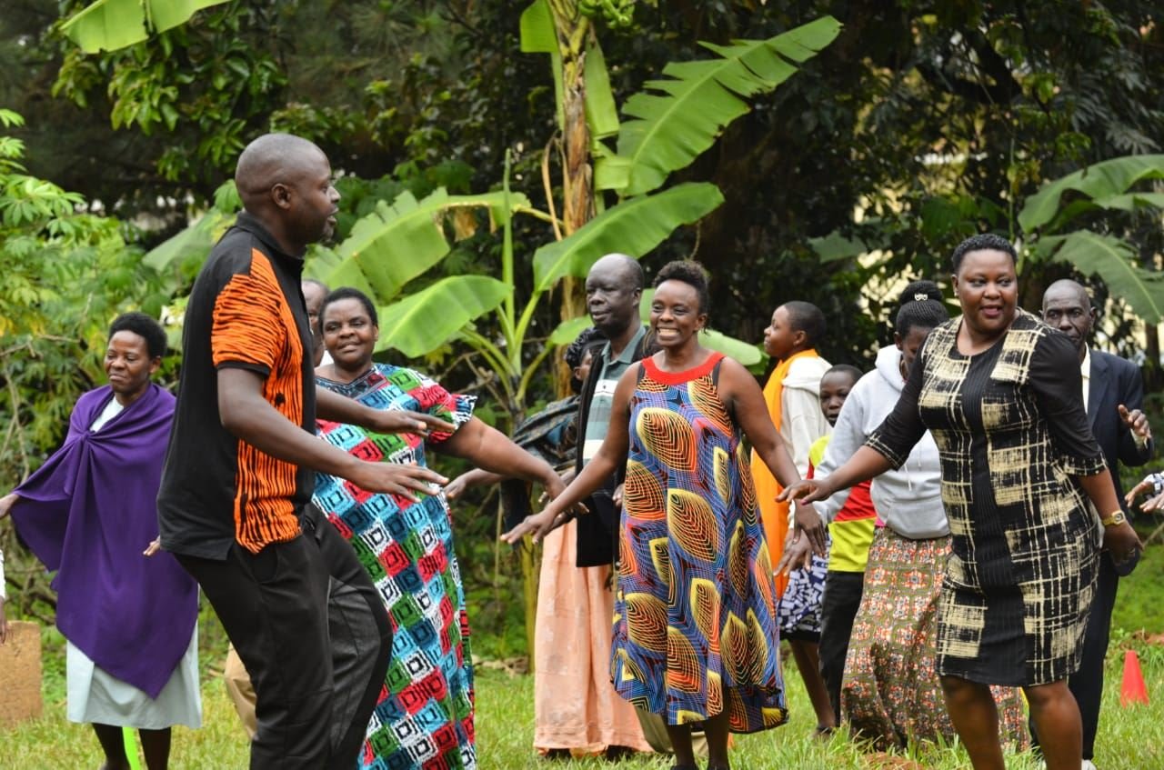 Community members join hands in a wide circle during a group activity outdoors.